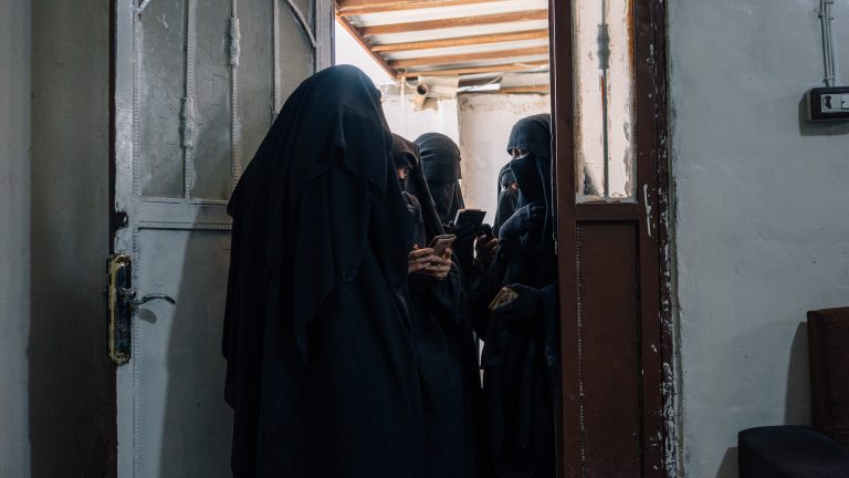 Women stand at a registration office at al-Hol camp, looking for documents in their phones they need to print to apply for permission to leave the camp.