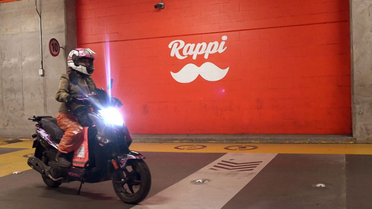 A motorcycle courier rides her bike past a Rappi sign while working in Bogota.