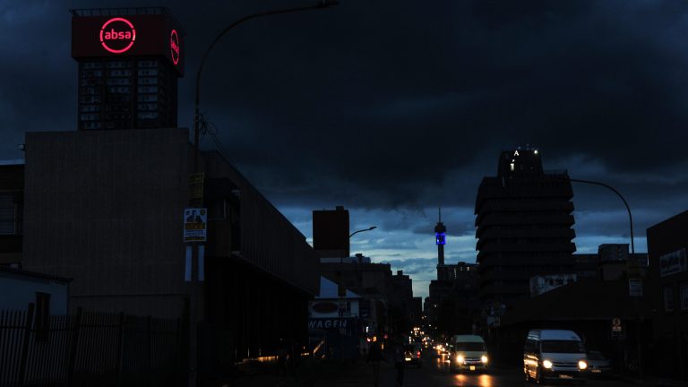 Vehicles travel along a darkened street without lighting during a loadshedding power outage period, in central Johannesburg, South Africa.