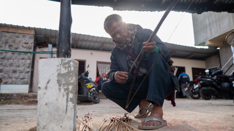 A photo of a man with a bow and arrow readying himself to play the sport of teer in India.