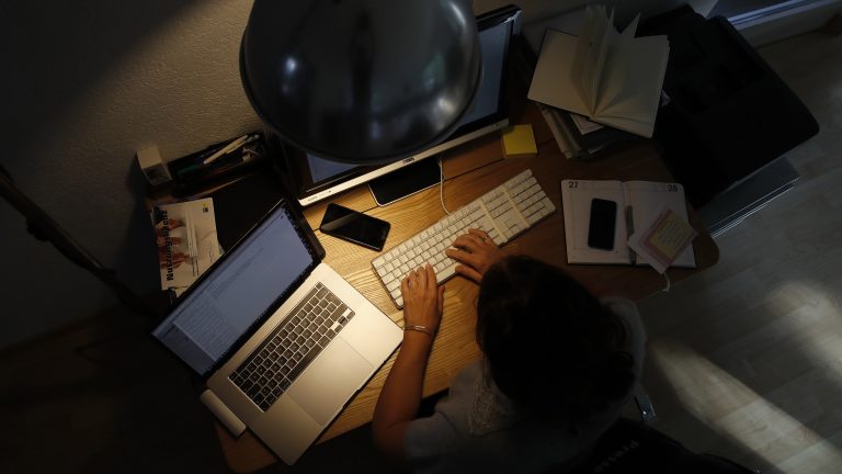 A woman works at a desktop computer at night in an arranged photograph.
