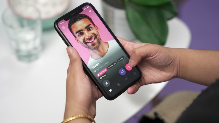 A photo of two hands holding a phone with the Muzz app open and showing a photo of a smiling man.