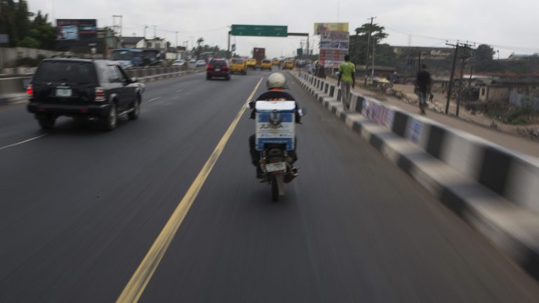 A photo of a delivery rider driving a motorbike down a highway in Lagos, Nigeria.