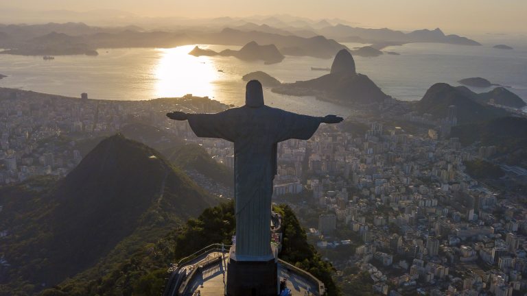 A photo of the statue of Christ the Redeemer as seen from above during sunrise or sunset in Rio de Janeiro, Brazil.