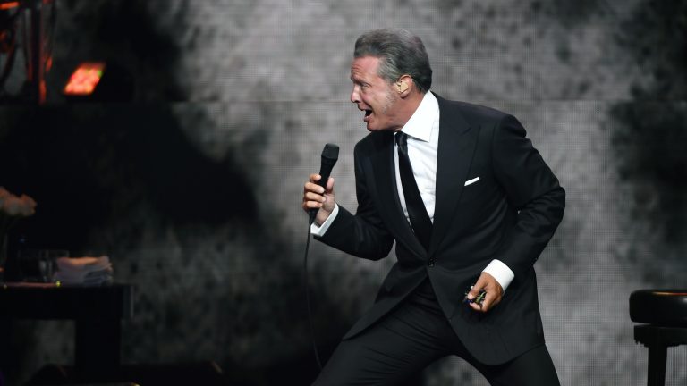 A photo of Mexican singer Luis Miguel performing during a concert in a black suit.