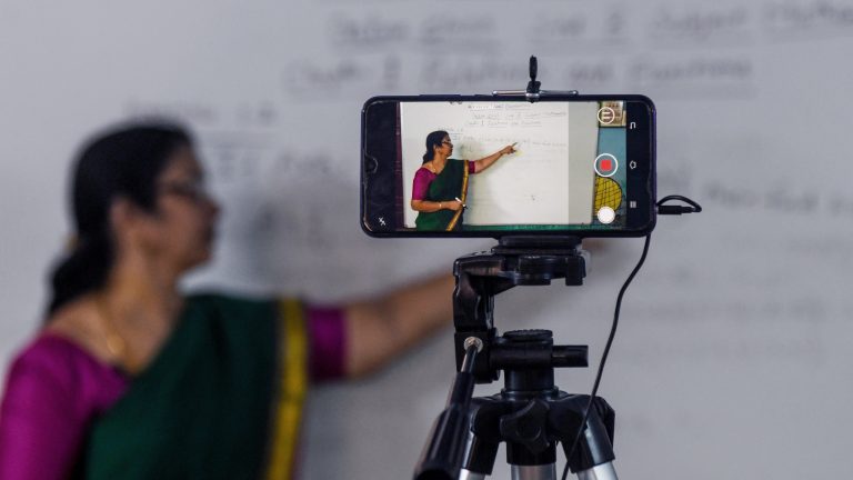 This photo shows a teacher recording a lesson using a phone and tripod.