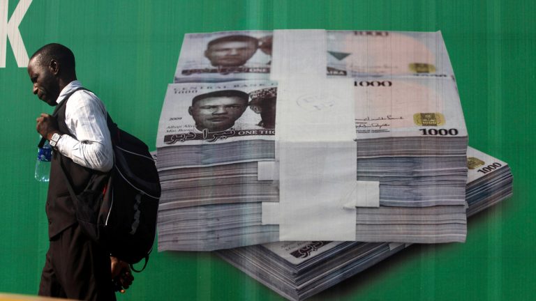 A man walks past a promotional banner showing a photograph of a pile of Nigerian naira along a road in Lagos.