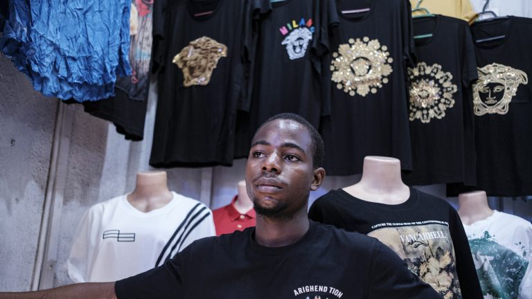 A photo of a man standing in a store with a display of t-shirts behind him.