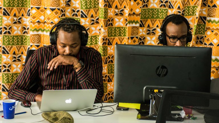 Two tech entrepreneurs work on computer against a bright yellow patterned backdrop.