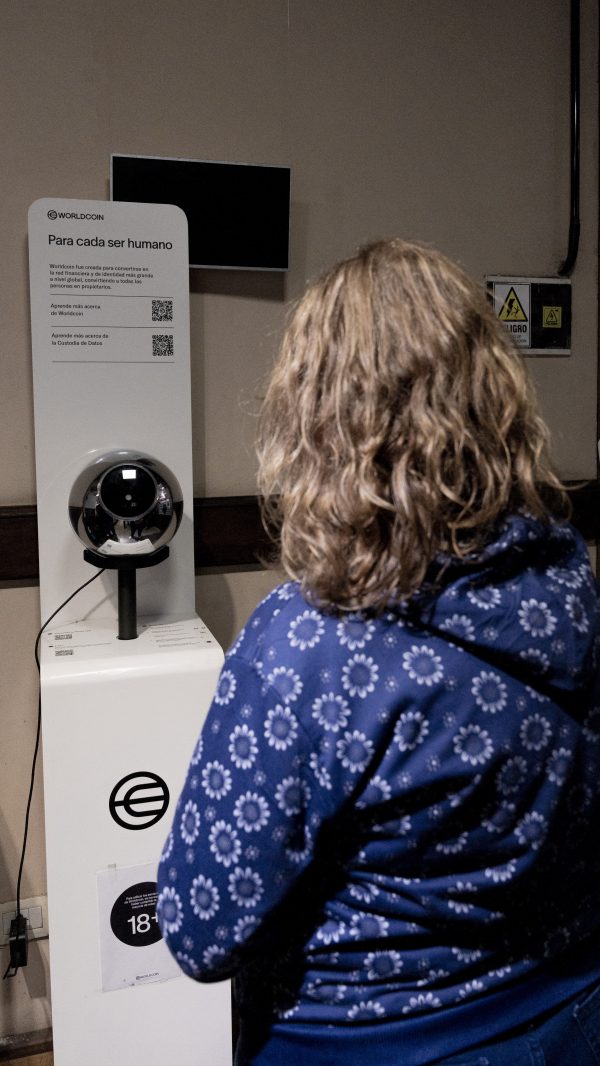 A woman stands in front of a sperical Worldcoin iris scanner.