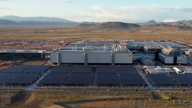A photograph from a drone video showing a large factory complex in the middle of the desert.
