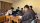 A photograph showing a group of young men seated around desks using their laptops inside a dorm room.