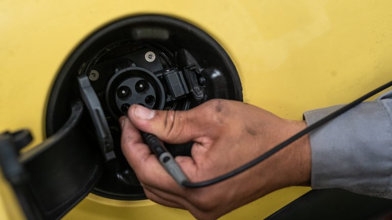 A photo of a close up of an electric vehicle charging port with a hand holding a mechanical tool.