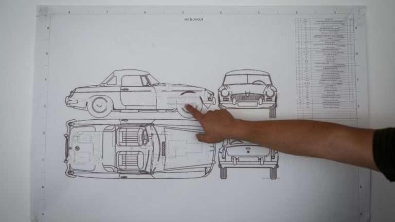 A photo of a hand pointing towards a technical drawing of a car