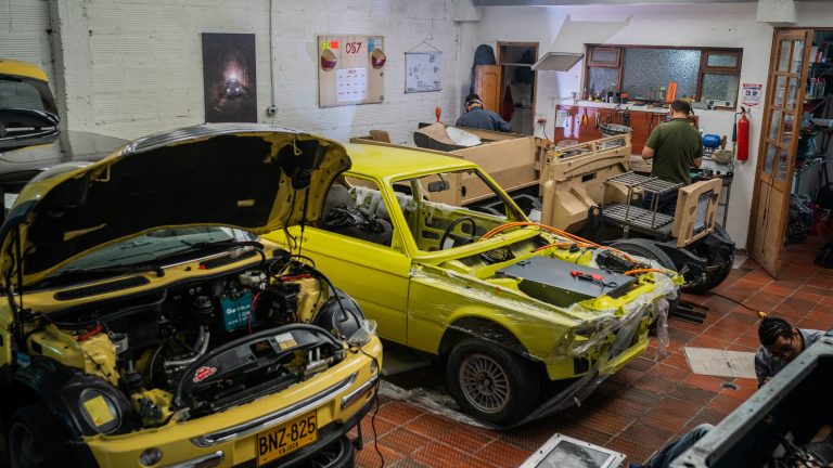 A photo of a mechanical car repair garage. There are two yello vehicles with their parts disassemebled.