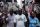 A portrait of a man, standing in the middle of a busy market in Lagos, as other people rush by him in a blur.